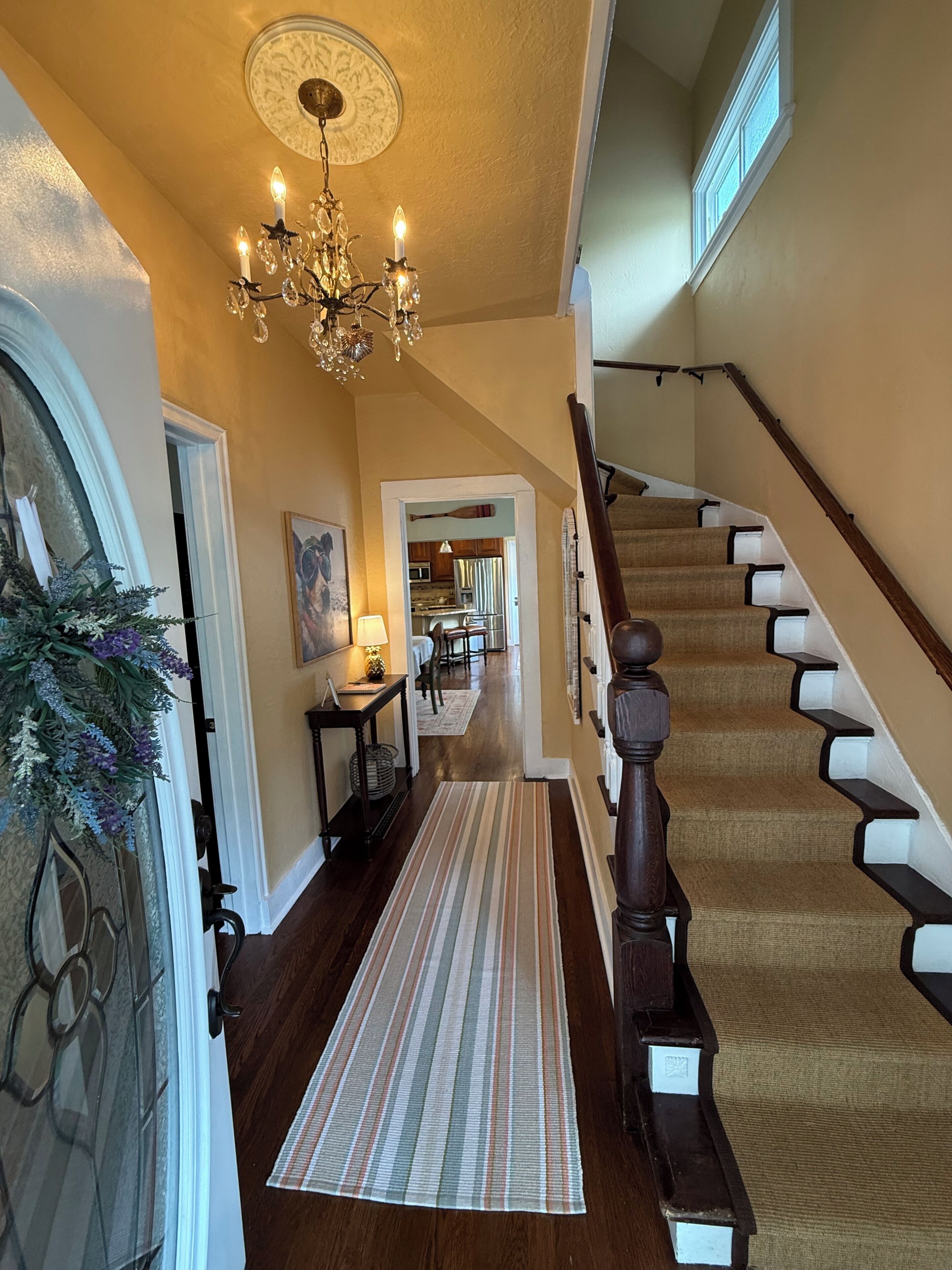 A hallway with a chandelier, a staircase, and a view into the kitchen.