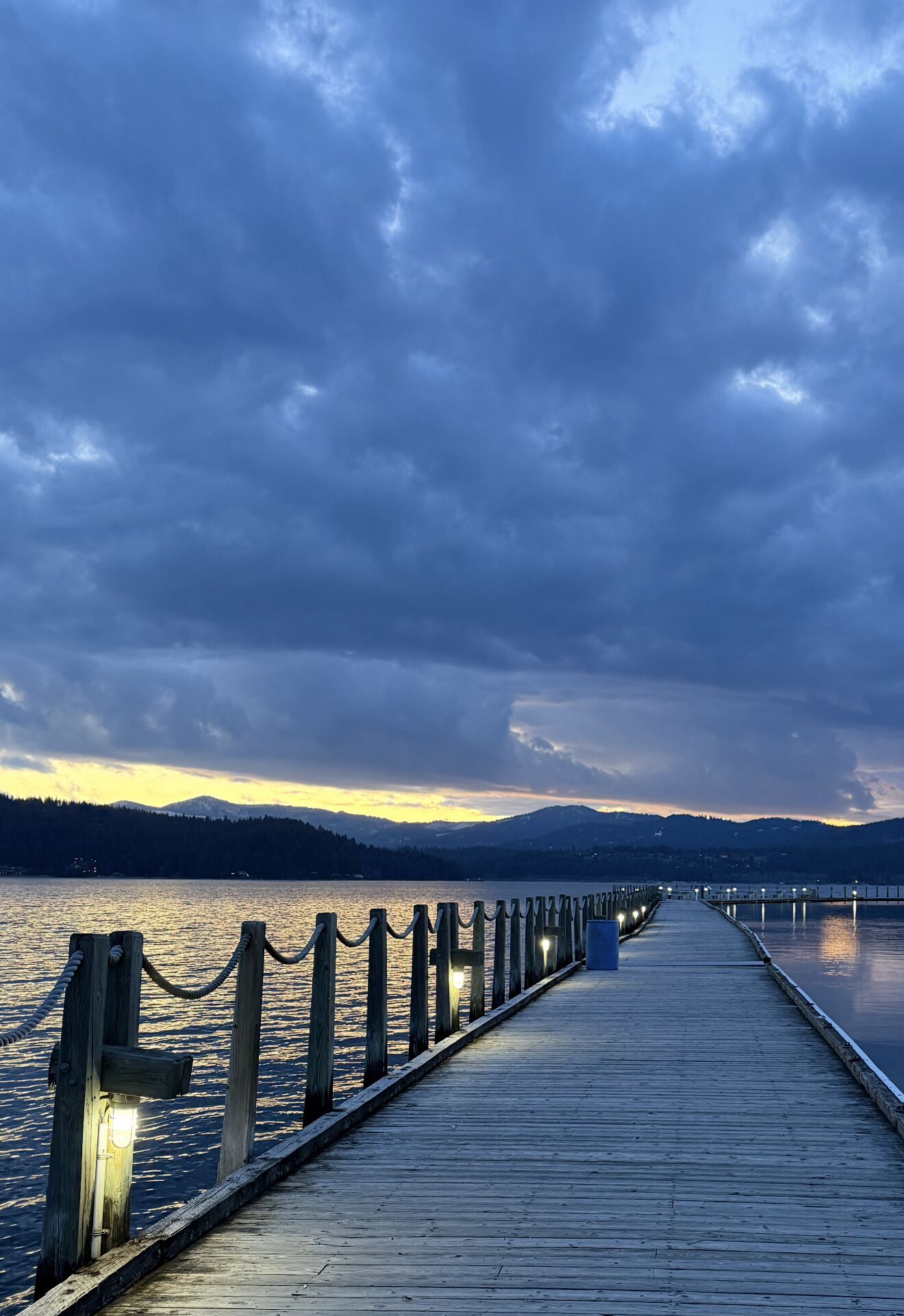 A wooden pier extending into a body of water, with a chain barrier on one side and a wooden railing on the other.