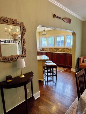 A spacious living area with a wooden floor, a dining table with a lamp, a bench, and a large mirror.