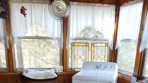 Un acogedor interior de cabaña con un sofá rojo, una lavadora, una mesita y un ventanal con cortinas.