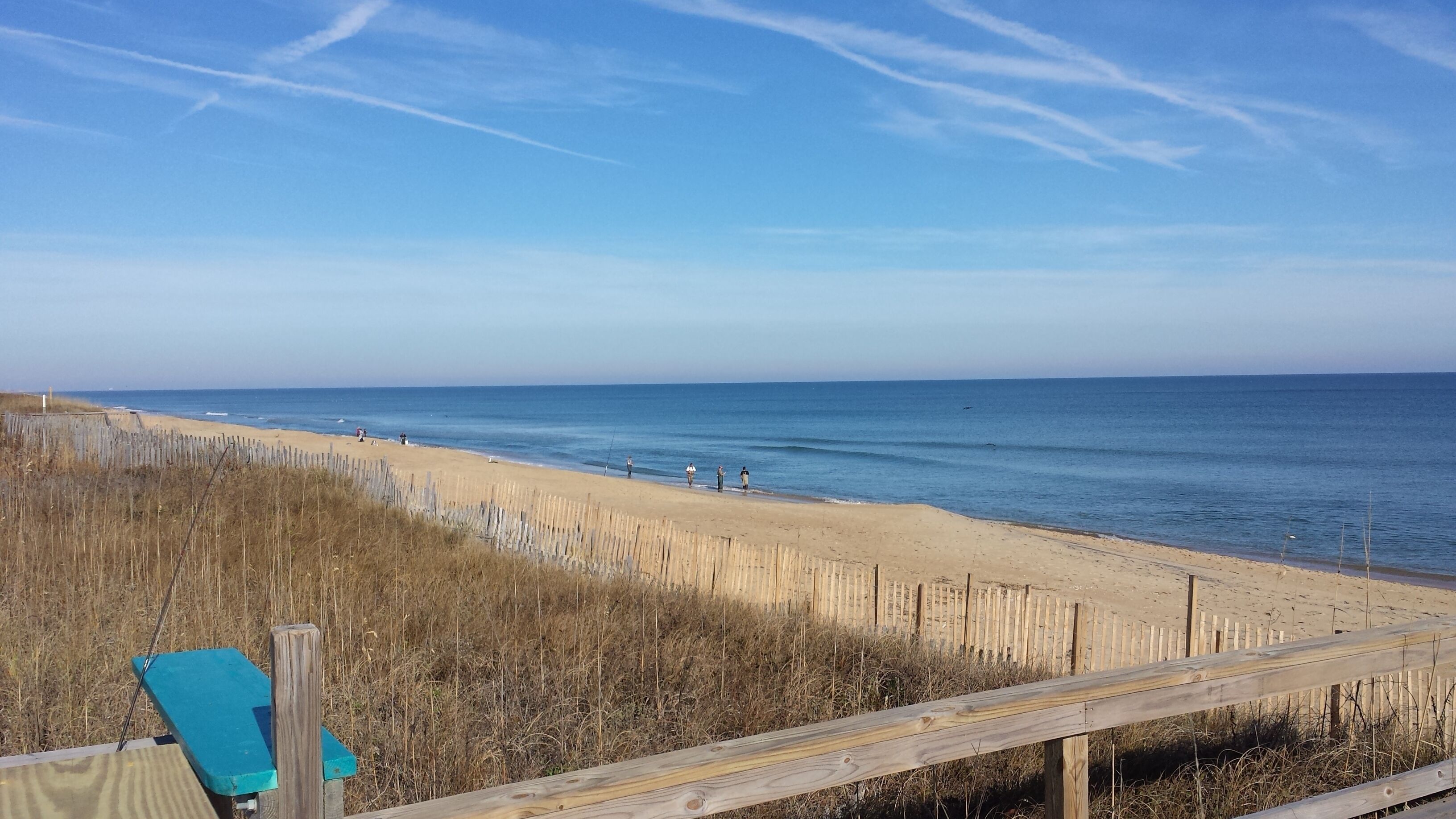 Ein Strand mit einer Holzlattenveranda und einem blauen Stuhl.
