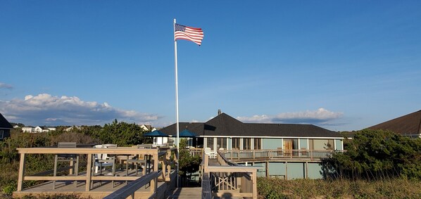 A beach house with a deck, a flagpole with an American flag, and a view of the ocean. - OCEANFRONT☆One level living w/ramp access to house & dune deck. Walk to dining! (Kitty Hawk)