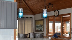A kitchen with wooden cabinets, a granite countertop, hanging pendant lights, a clock, and a window with a view. - OCEANFRONT☆One level living w/ramp access to house & dune deck. Walk to dining!  (Kitty Hawk)