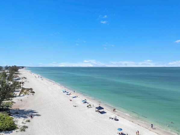 A beach with clear blue water, a sandy shore, and a few umbrellas.