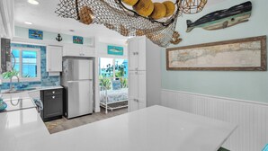 A modern kitchen with white cabinets, a stainless steel refrigerator, and a dining area with a white table.