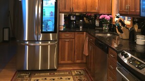 A kitchen with wooden cabinets, stainless steel appliances, a refrigerator with a digital display, a coffee maker, and a rug with a bear design. - lake George Adirondack Chalet  (Lake George)