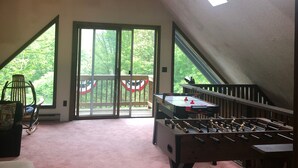 A spacious attic room with a foosball table, a rocking chair, and large windows offering a view of greenery. - lake George Adirondack Chalet  (Lake George)