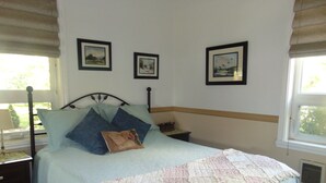 Una cama bien hecha con colcha, dos almohadas y una mesita de noche con lámpara. Encima de la cama hay tres cuadros enmarcados en la pared.