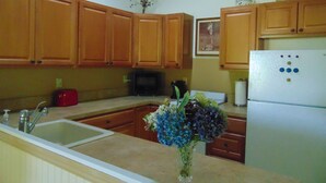 Una cocina con armarios de madera, un lavabo, microondas, refrigerador y un florero con flores en la encimera.
