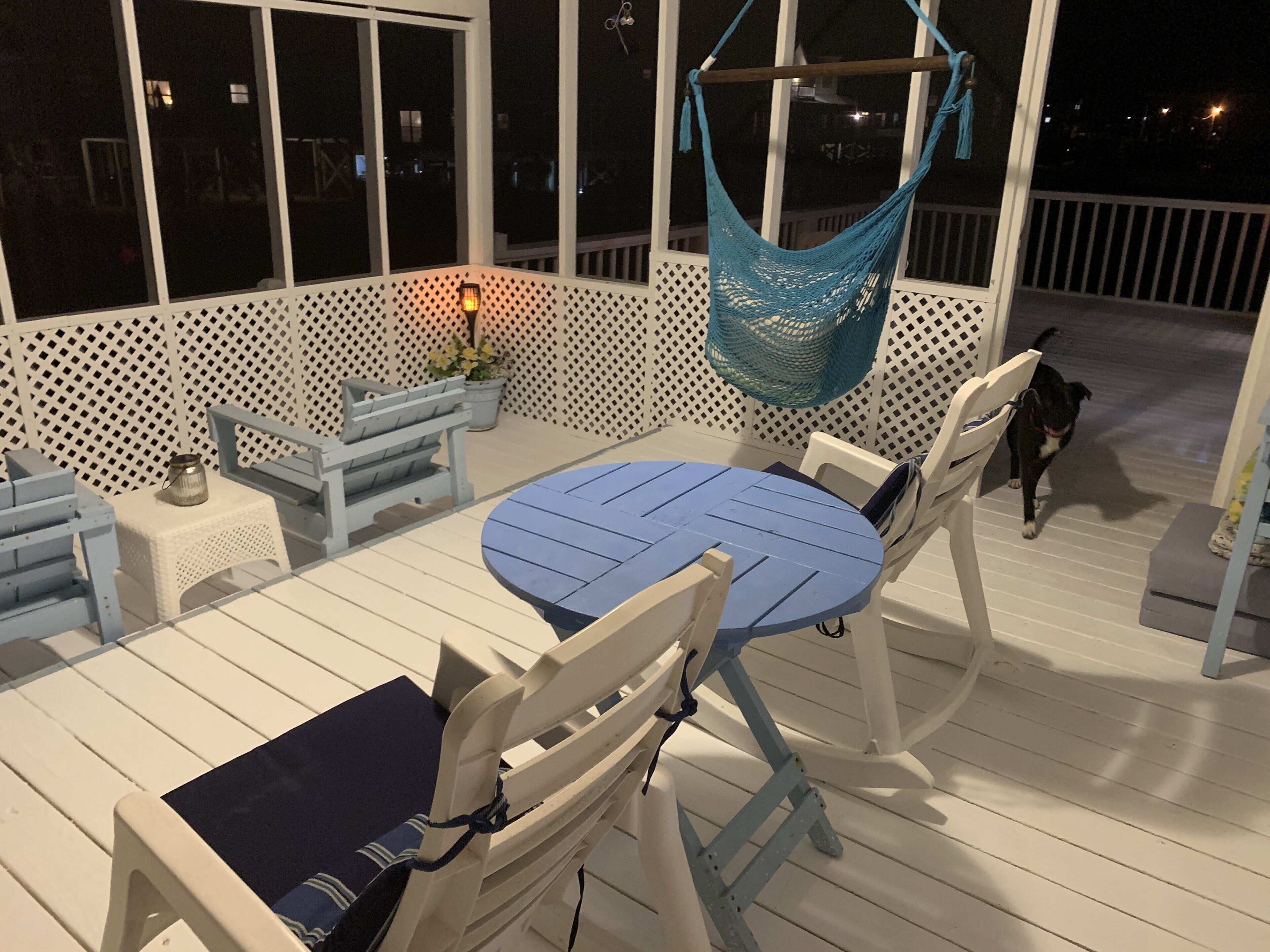 A covered outdoor seating area with a round table and chairs, a hammock, and a small table with a lantern.