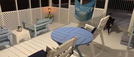 A covered outdoor seating area with a round table and chairs, a hammock, and a small table with a lantern.