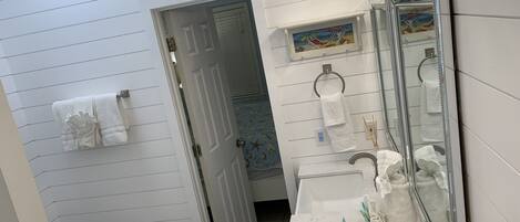 A bathroom with a toilet, sink, and mirror. There is a towel rack with towels and a painting above the mirror.