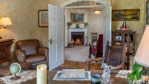 Un salon chaleureux avec une cheminée, un fauteuil en cuir et une table basse sur laquelle sont posés un livre et une bougie.