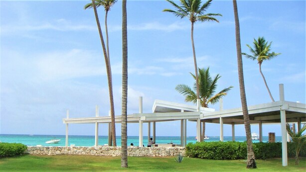 A covered outdoor area with palm trees, a stone wall, and a view of the ocean. - Playa Turquesa, Beachfront, Ocean view, pool, 2 Bd. Luxury Condo, Wifi, Smart TV (Bavaro)