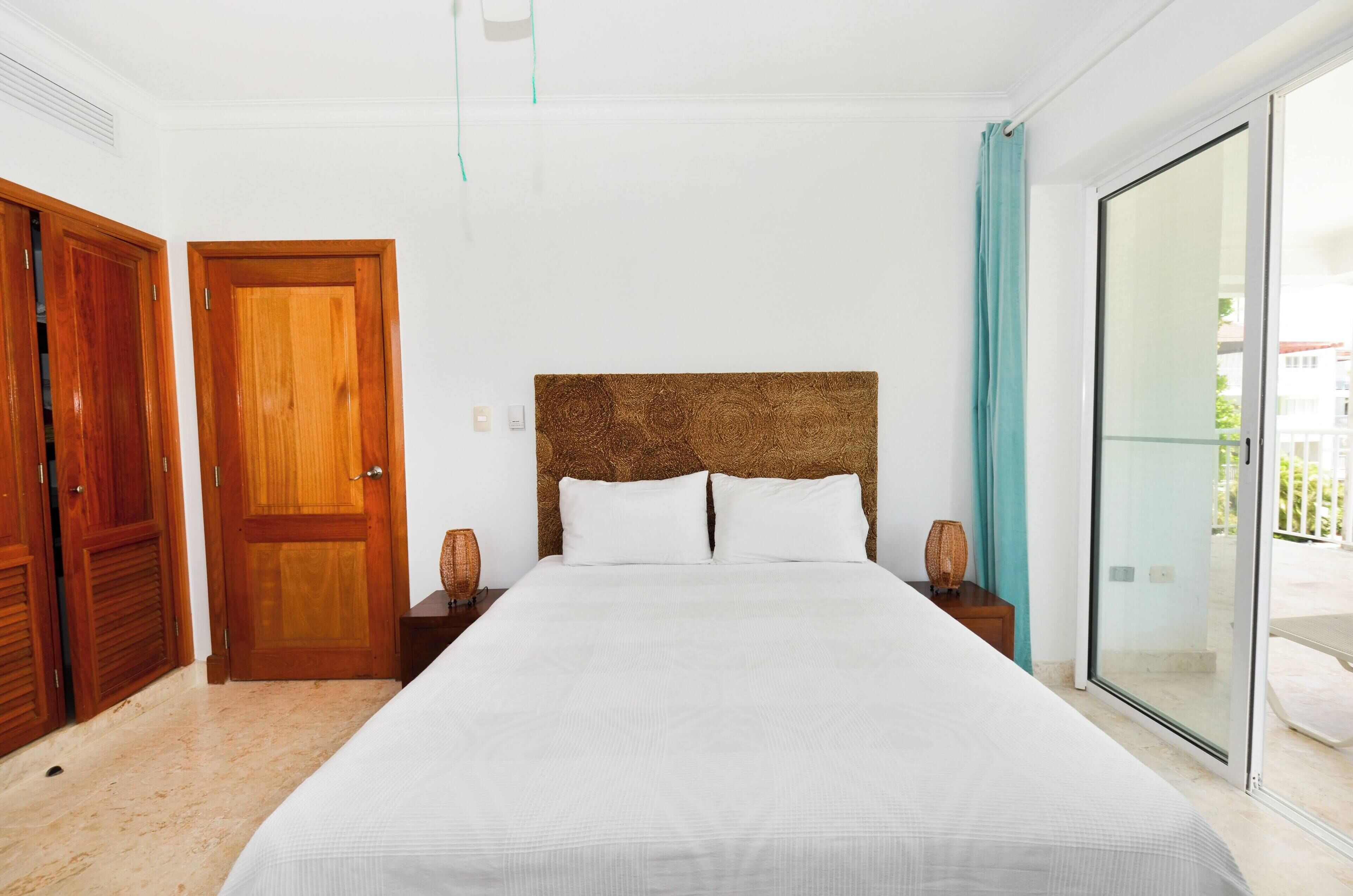 Une chambre à coucher avec un grand lit, des portes en bois, une fenêtre avec des rideaux et une vue sur l’extérieur.
