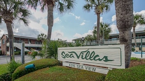 Placa para Sea Villas, com vista para o mar, um edifício de tijolos e palmeiras.