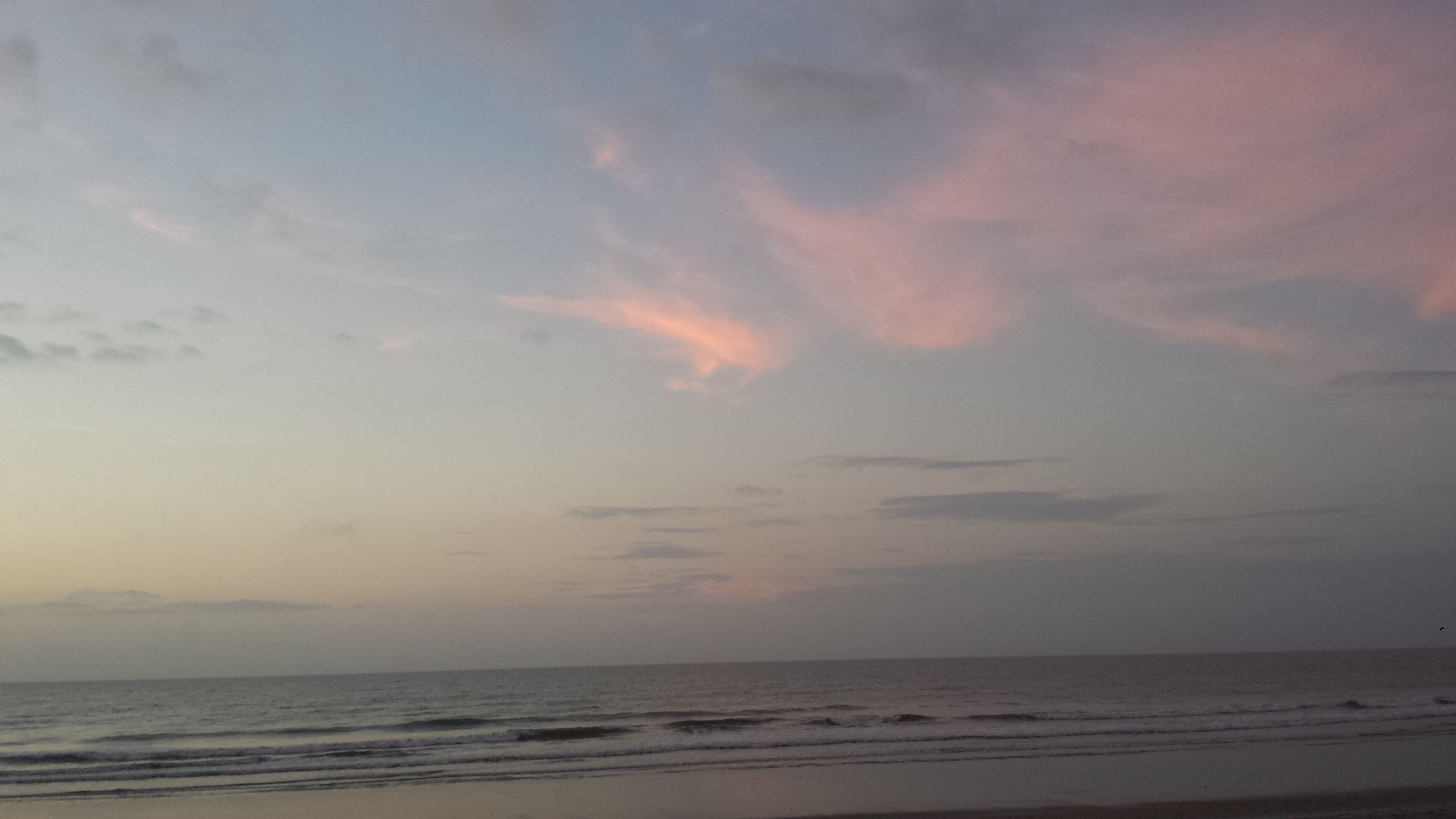Une plage avec une mer calme et un ciel nuageux.