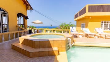 Un espace piscine doté d’un jacuzzi, de chaises longues et offrant une vue sur l’océan.