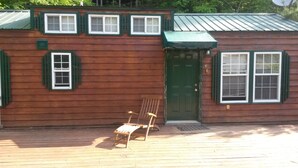 A wooden cabin with a green door, two windows with shutters, and a bench outside.