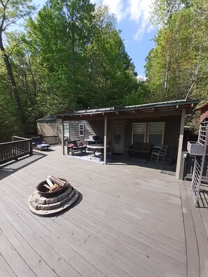 A wooden deck with a fire pit, outdoor furniture, and a covered patio area.