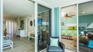 Amplia sala de estar con puerta corrediza de vidrio que da a un dormitorio con cama y ventilador de techo.