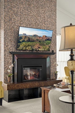 A fireplace with a flat-screen TV mounted above it, a yellow chair, and a lamp on a table.