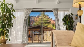 A room with a view of a canyon, a wooden table, a beige sofa, and a lamp. - Panoramic Red Rock Views | Walk to Uptown (Sedona)