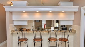 A kitchen with a bar area, white cabinetry, and four bar stools. - beautiful Home 98 steps from the beach just off Thomas drive (Panama City)