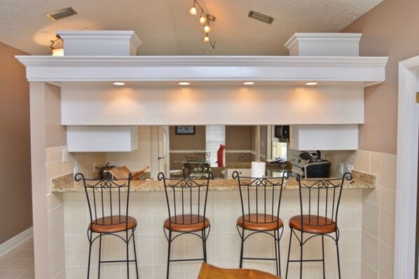 A kitchen with a bar area, white cabinetry, and four bar stools.