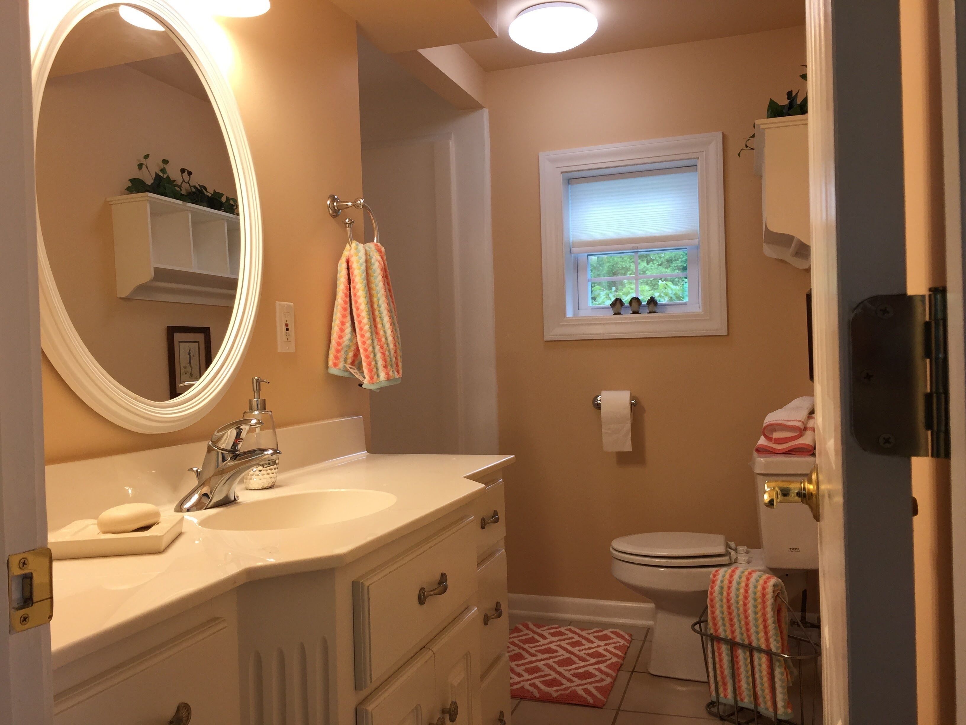 A bathroom with a vanity, sink, mirror, toilet, and a window with a view of greenery.