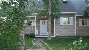 A house with a stone pathway leading to the front door, surrounded by greenery and a small stone wall. - Vineyard Haven, Quiet Setting Just Minutes from Ferry and Bus (Vineyard Haven)