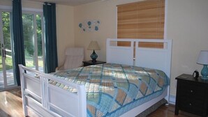 A bedroom with a bed, a chair, a nightstand, a lamp, and a window with blinds. - Vineyard Haven, Quiet Setting Just Minutes from Ferry and Bus (Vineyard Haven)