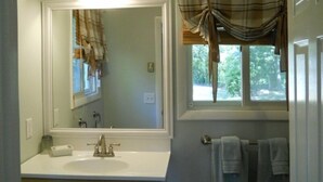 A bathroom with a large mirror, a sink, a window with curtains, and a towel rack. - Vineyard Haven, Quiet Setting Just Minutes from Ferry and Bus (Vineyard Haven)