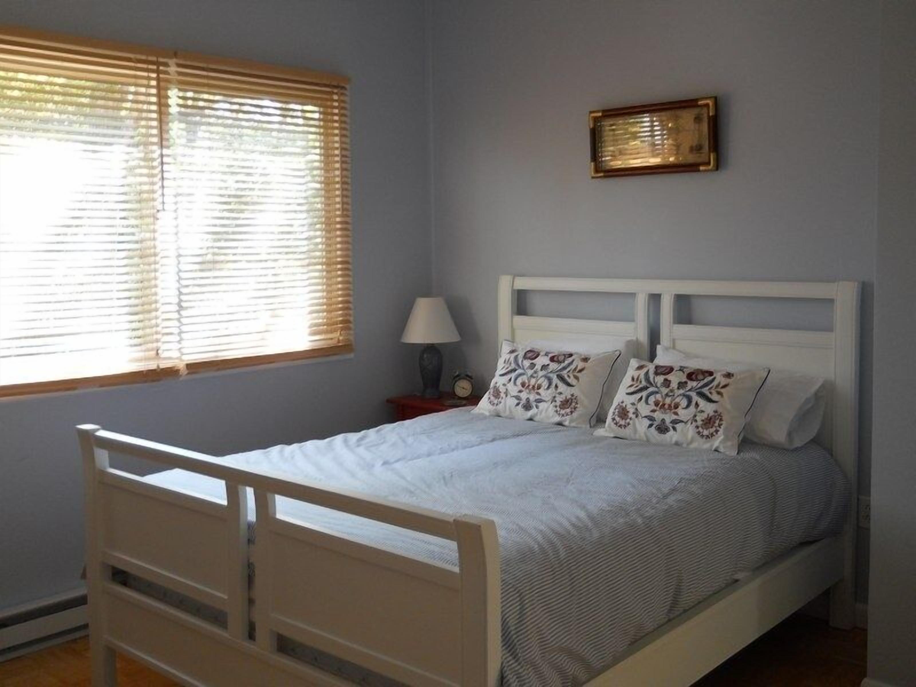 A bedroom with a bed, a nightstand, a lamp, and a window with blinds.