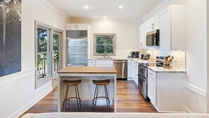 A modern kitchen with white cabinetry, stainless steel appliances, and a wooden island with bar stools. - AMAZING Golf Views of Turtle Point 18th Hole! Pool Access! (Kiawah Island)