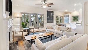 A spacious living room with a fireplace, a ceiling fan, and a view of the backyard through large windows. - AMAZING Golf Views of Turtle Point 18th Hole! Pool Access! (Kiawah Island)