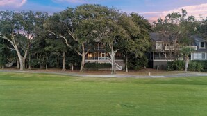 A two-story house with a front porch, surrounded by trees and a well-maintained lawn. - AMAZING Golf Views of Turtle Point 18th Hole! Pool Access! (Kiawah Island)