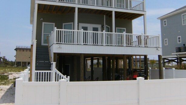 Ein zweistöckiges Strandhaus mit einem Balkon in jeder Etage, einer Veranda und einem sandigen Strand im Hintergrund.