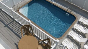 Ein Swimmingpool mit Liegefläche, umgeben von weißen Liegestühlen und einem Tisch.
