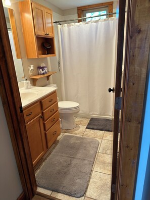 A bathroom with wooden cabinets, a toilet, a shower curtain, and two rugs. - looking for some peace and quiet? You'll find no better place at the Lake. (Sunrise Beach)