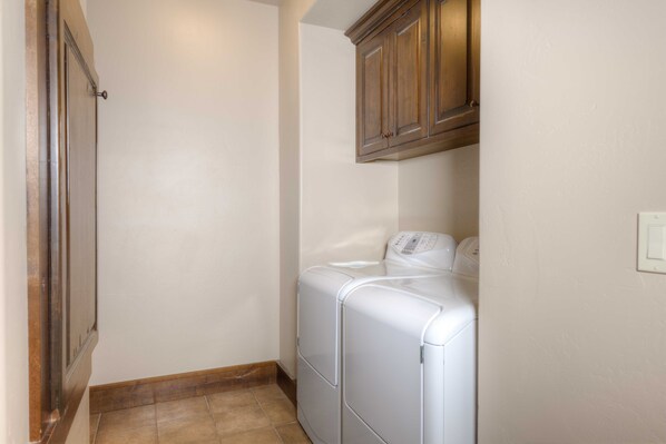 A laundry room with a washing machine and dryer, wooden cabinets above, and a tiled floor.