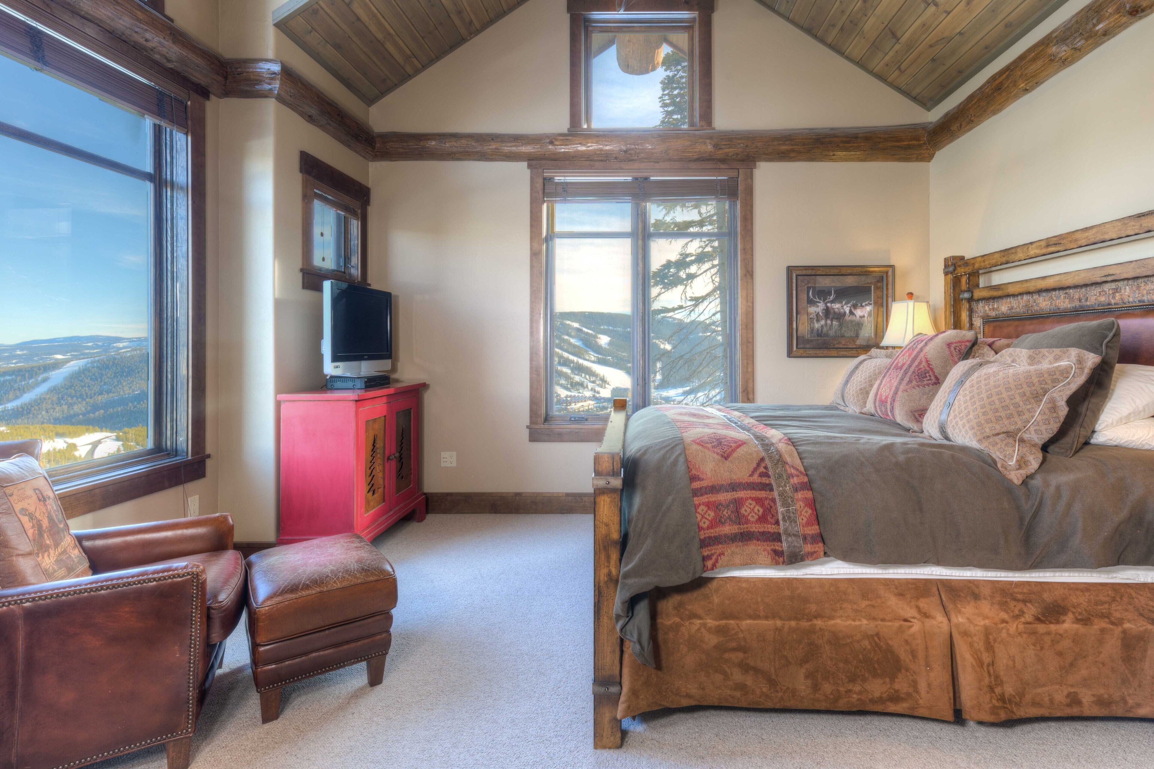 Une chambre à coucher avec un grand lit, une télévision, une armoire rouge et une fenêtre donnant sur les montagnes.