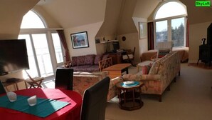 Ein geräumiges Wohnzimmer mit hohen Decken, einem Essbereich mit einem roten Tisch und einer Sofagarnitur.