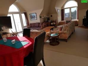 Amplia sala de estar con techo alto, comedor con mesa roja y un conjunto de sofás.
