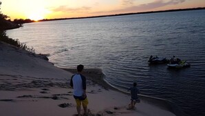 Ein Strandbild mit Sonnenuntergang, Sandstrand und Personen in Wassernähe.