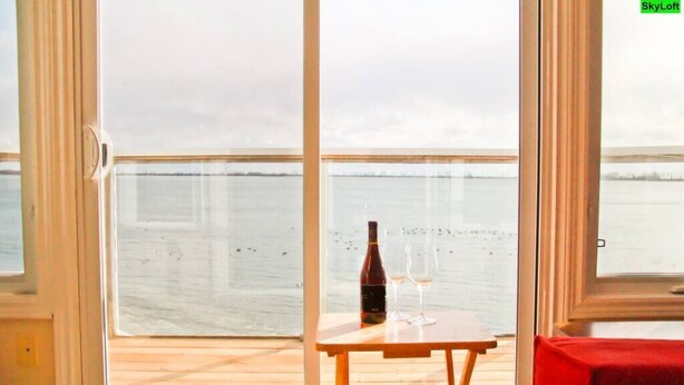 Ein Balkon mit Tisch und einer Weinflasche, mit Blick auf ein Gewässer.