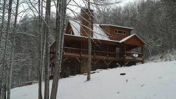Una cabaña de troncos con balcón, rodeada de árboles cubiertos de nieve.