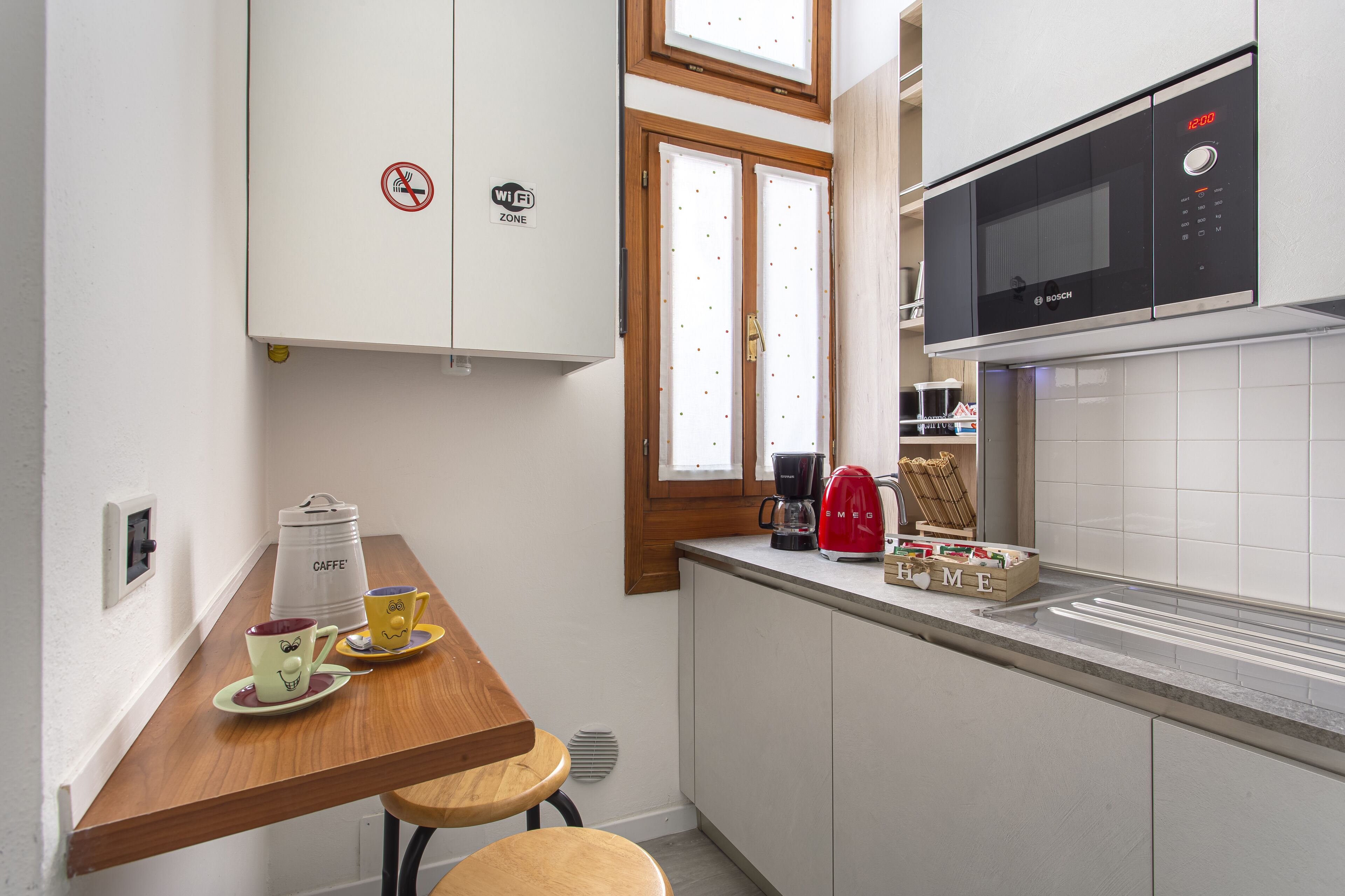 A compact kitchen with a microwave, coffee maker, and a small dining area with stools.