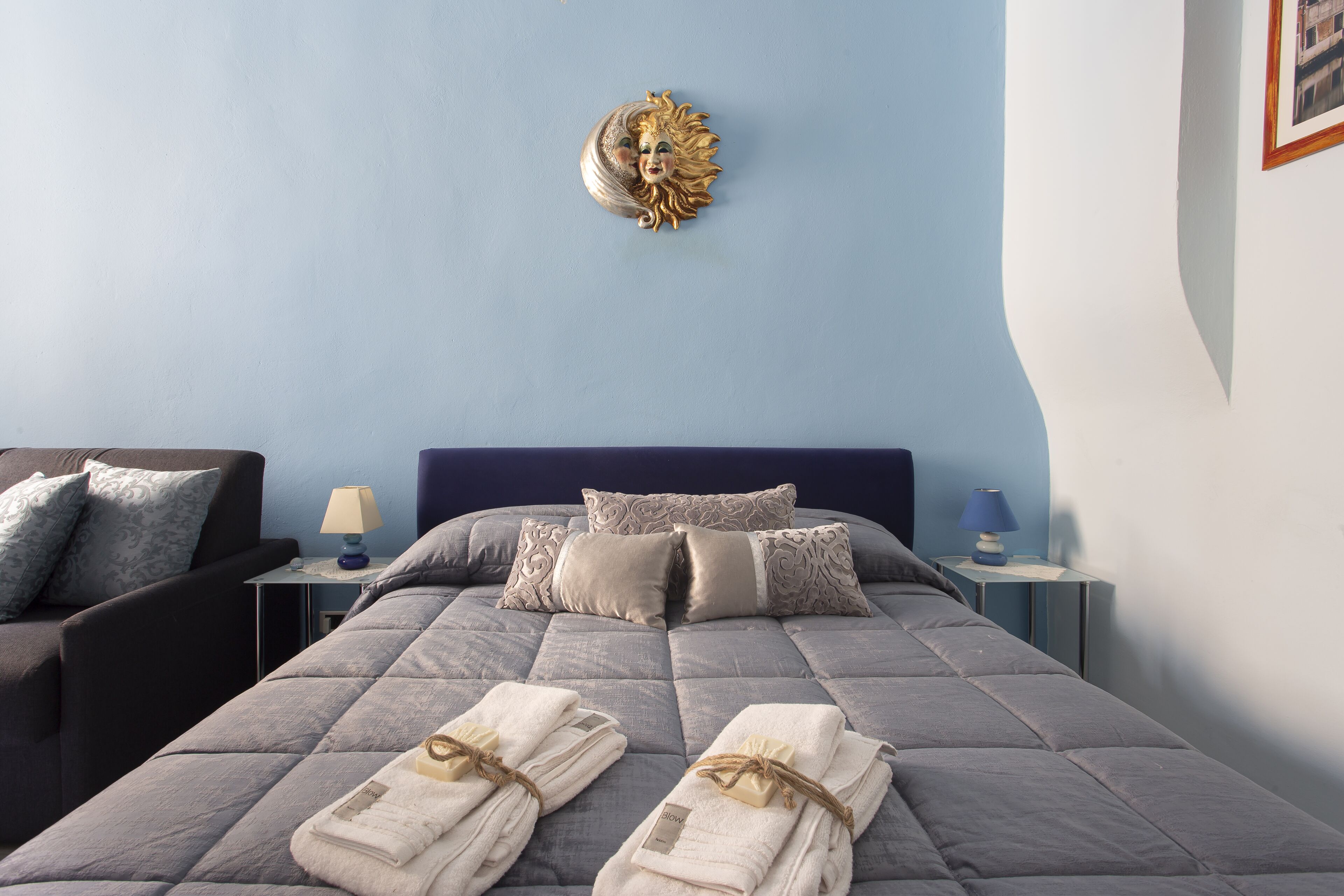 Una cama bien hecha con almohadas, una lámpara de noche y un adorno de pared.