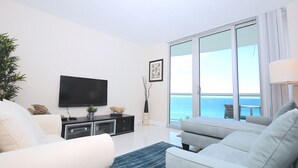 Una sala de estar moderna con un televisor de pantalla plana, un sofá, una mesa de centro y vista al océano a través de puertas corredizas de vidrio.
